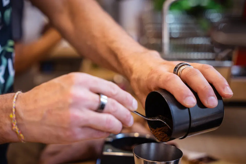 Hands dosing freshly ground coffee.